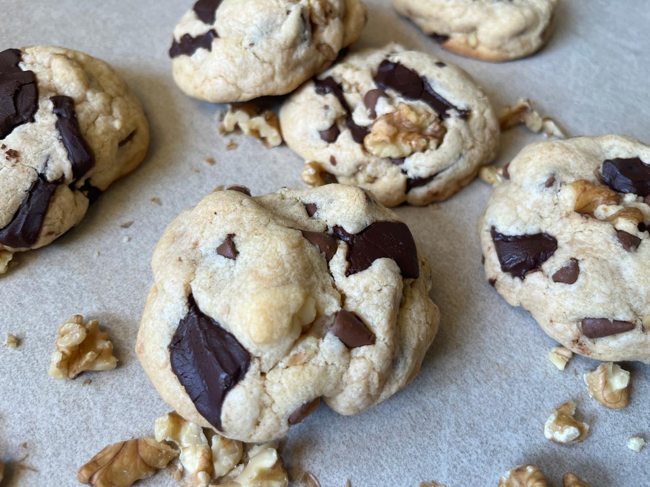 A close up of a cookie with huge bits of smooth, deep, and creamy dark chocolate with bits of chocolate chips and walnuts. It's practically calling out for you to taste it